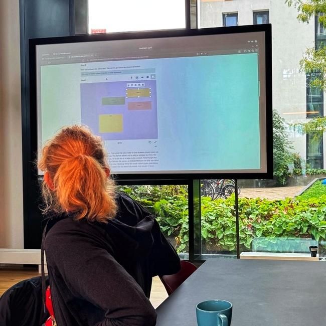 Woman watching a large screen that shows the #H5P idea board content type.