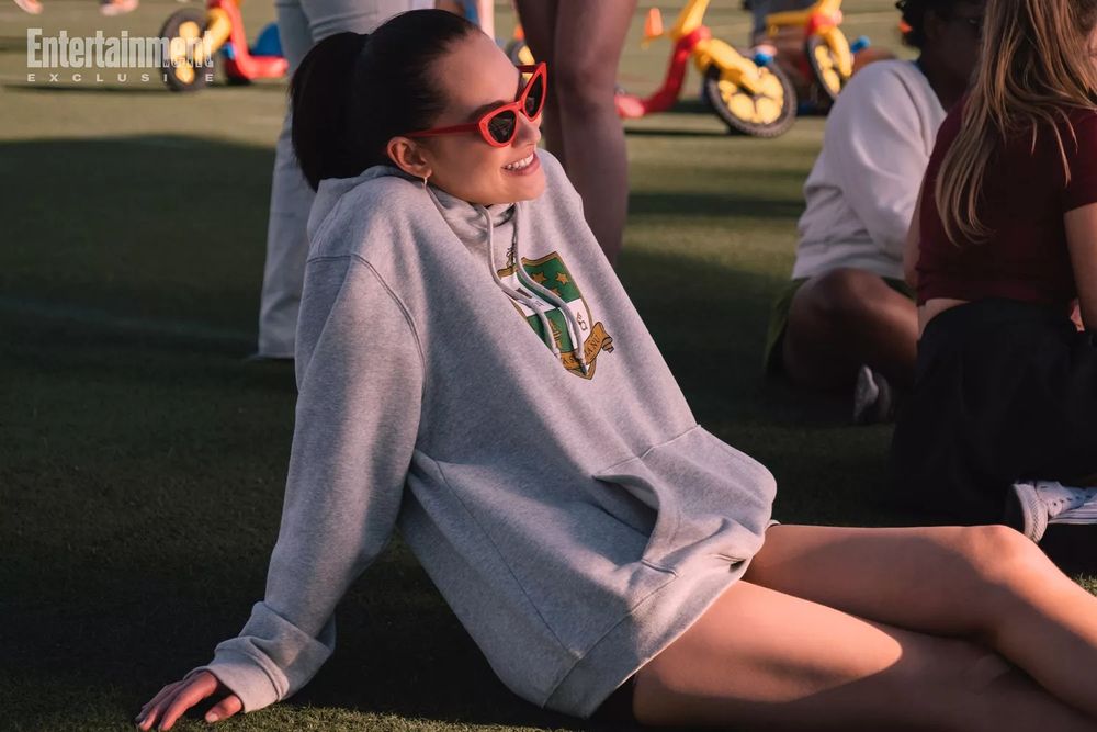 Belly lounging on AstroTurf wearing red sunglasses and a fraternity hoodie. Tricycles are visible in the background.