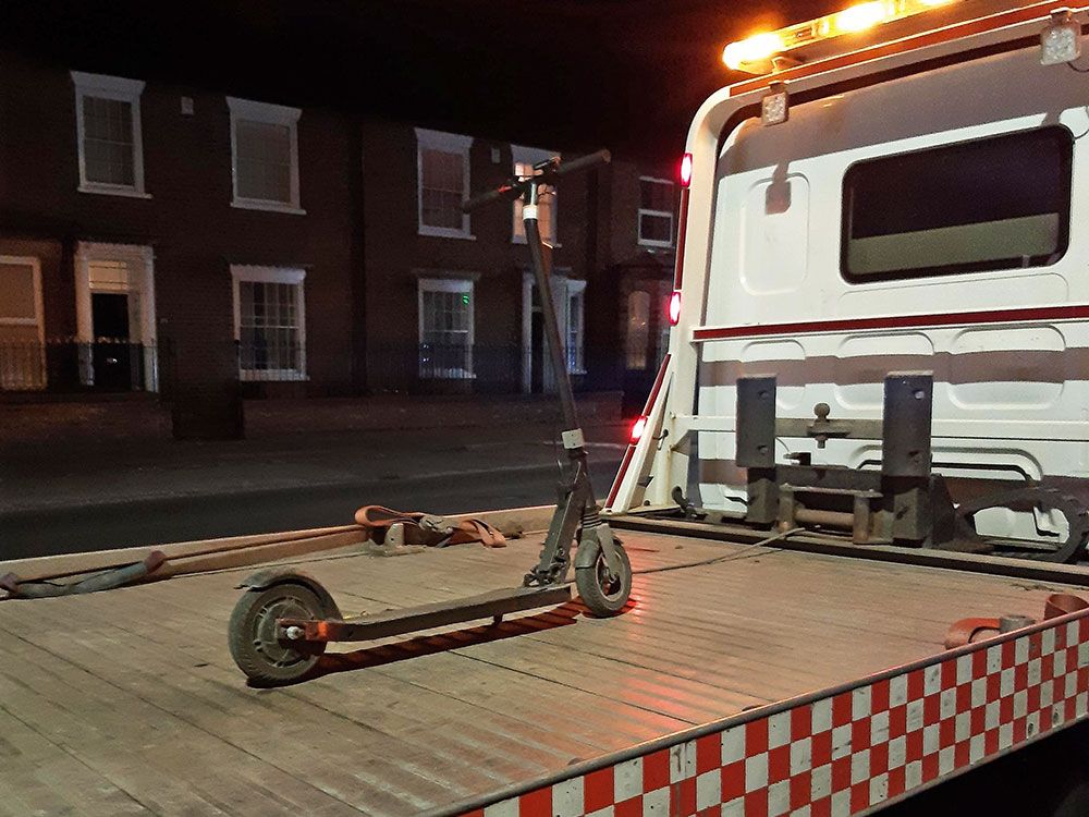 Another single e-scooter sitting (securely) on a very long low-loader (but it is night this time). 