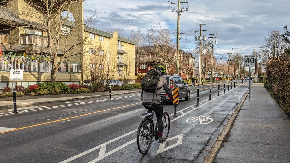 A view to the East of a person riding a bike in the Caledonia Avenue protected bike lane. Photo taken from the intersection of Caledonia Avenue and Quadra Street.