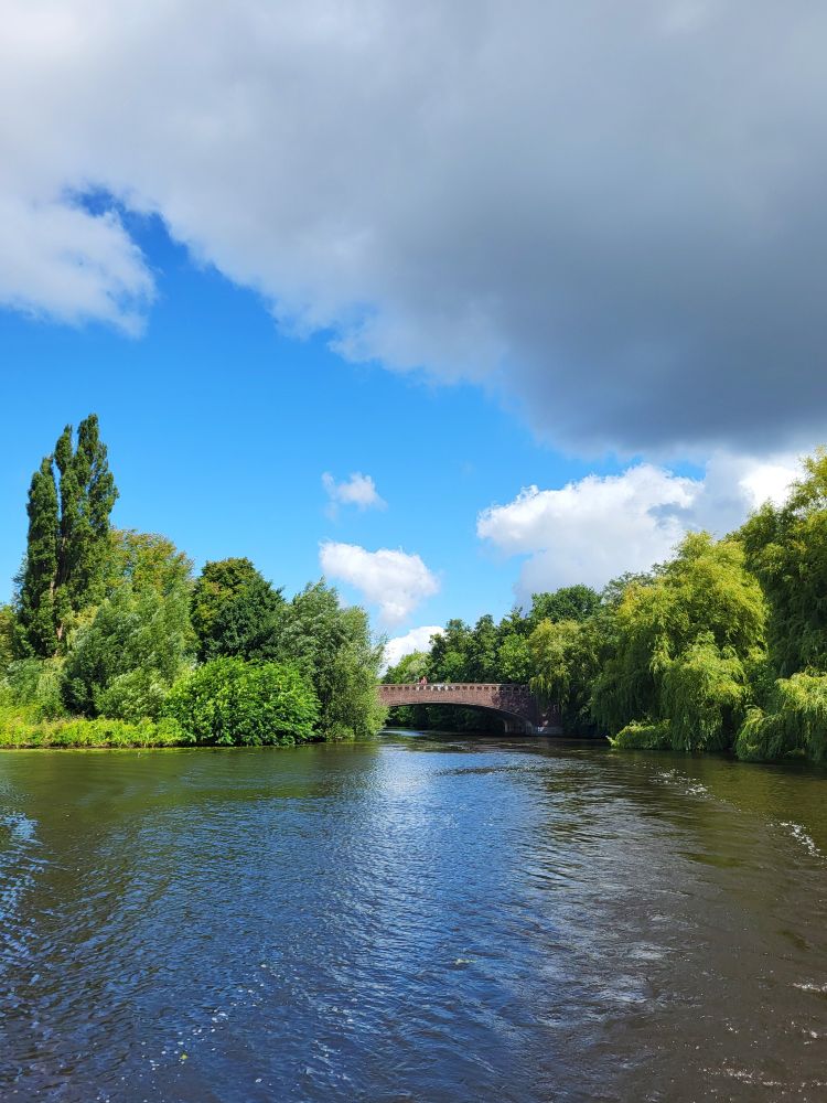 Blick auf die Alster. Im Hintergrund eine Steinbrüche. Links und rechts von der Brücke sind viele Büsche und Bäume. Der Himmel ist bewölkt. 