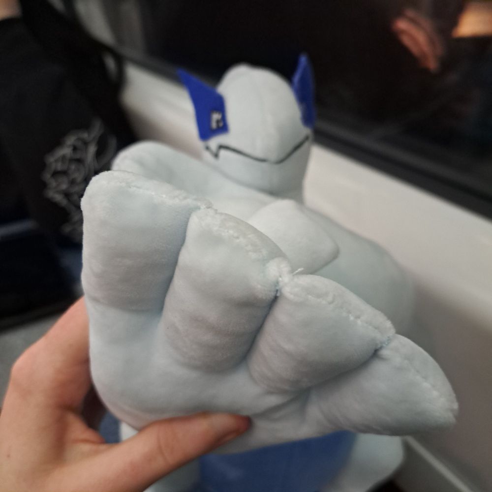 a lugia plush being held in a way that has it holding up four fingers to the camera, its other arm across its chest and throat.
