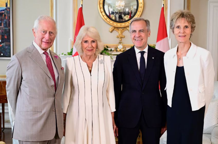 King Charles and Queen Camilla pose with Prime Minister Mark Carney and his wife Diana Fox Carney. King Charles wears a taupe suit with a single-breasted notched-lapel jacket, white shirt, and a red tie. 