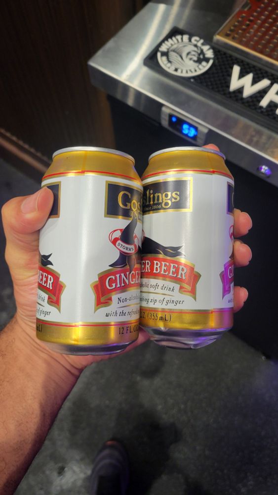 A man with large hands holding two cans of soda in one hand