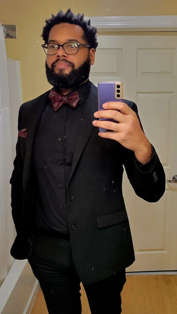 A man wearing a black suit with a black shirt and a bowtie