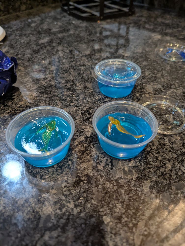 Blue jello shots with a plastic mermaid on top of them