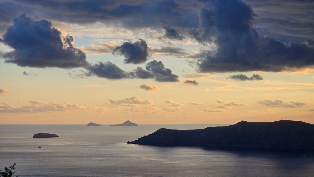 Tiny islands close to Santorini in the evening with some dark clouds in the sky. 
