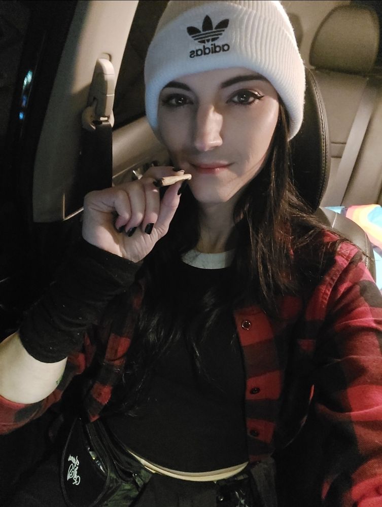 girl in black crop top and red flannel with a white beanie on is about to smoke a joint 