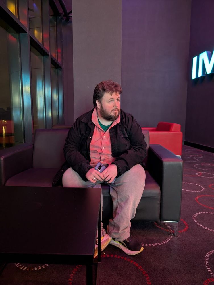 A picture of me sitting on a couch in a cinema lobby. I haven't noticed I've been snapped so I'm looking off into the distance