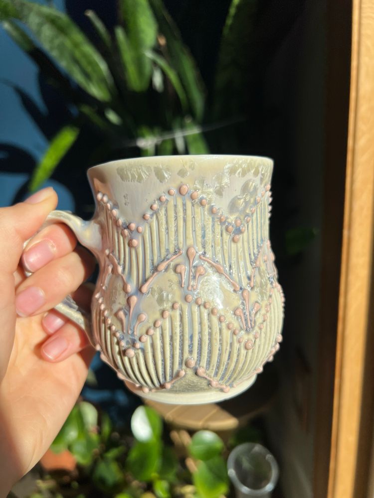 A purple and pink mug with silver crystals. It has a zig zag pattern made by slip trailing and carved lines