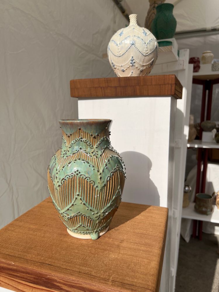 Two vases on two pedestals set up at an art fair. The first vase is turquoise and the second is white 