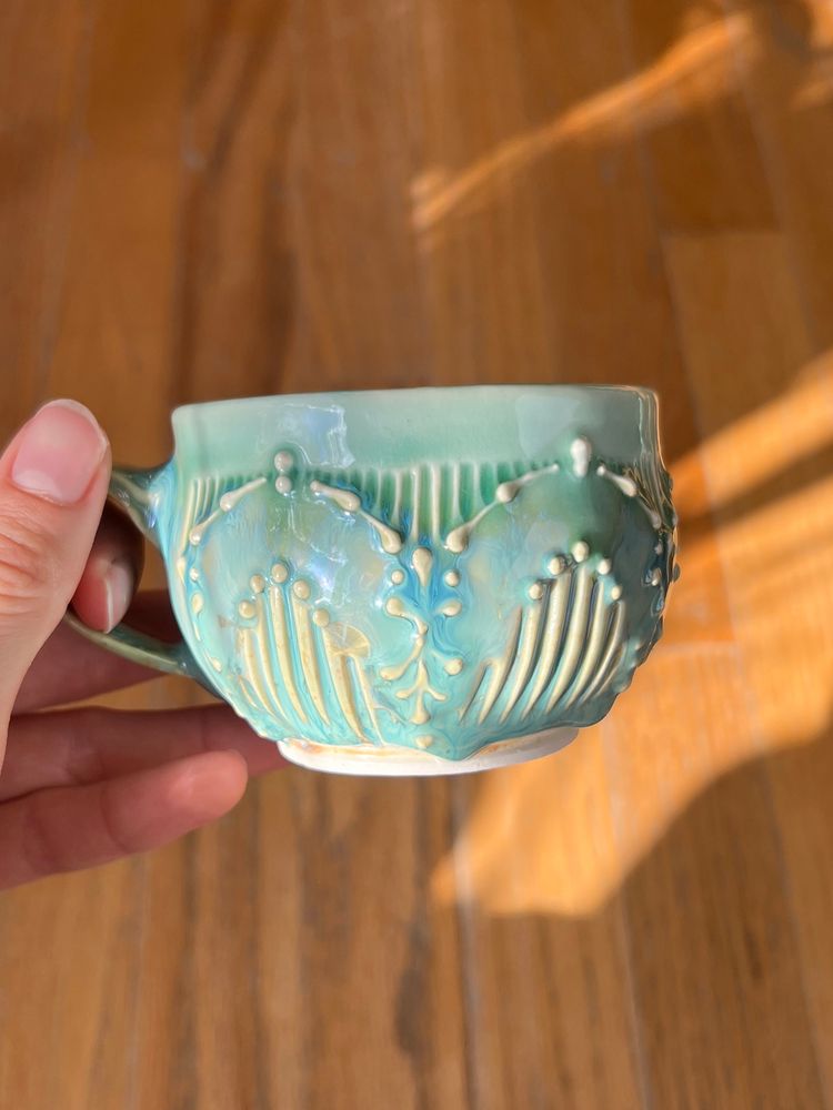 An opal teacup with zig zag pattern created by carved lines and botanical slip trailing 