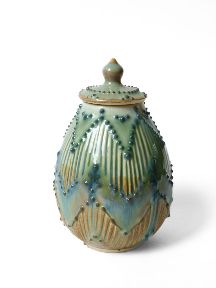 A jar with a zig zag pattern and colorful glaze that is a bit runny looking going from green at the top to blue to orange
