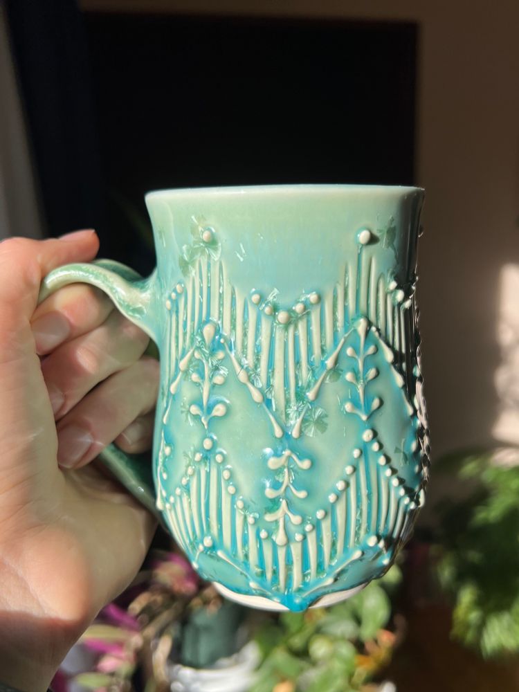a mug with a turquoise crystalline glaze and zig zag pattern made from carved lines and slip trailing 
