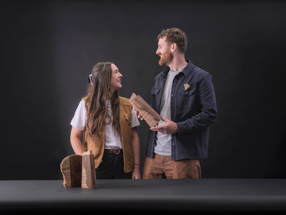 A man and woman smile at each other while holding a colorful wooden object. More wooden pieces are on the table in front of them.