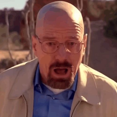 a bald man with glasses and a beard is wearing a blue shirt and a tan jacket