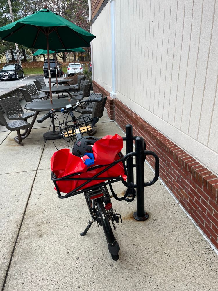 E-bike parked outside Whole Foods at a bike rack with big red harbor freight reusable bag on back rack 