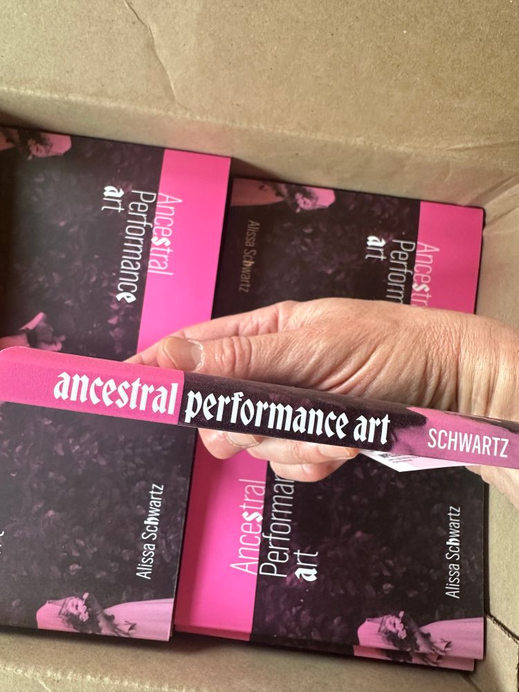 photograph of a box of paperback books, with a hand holding one of the books so that the spine can be seen. 