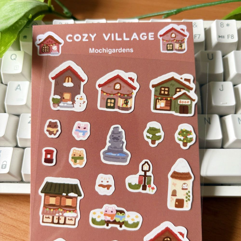 A sticker sheet featuring tiny christmas themed houses and buildings, as well as some trees, a fountain and various tiny cats!