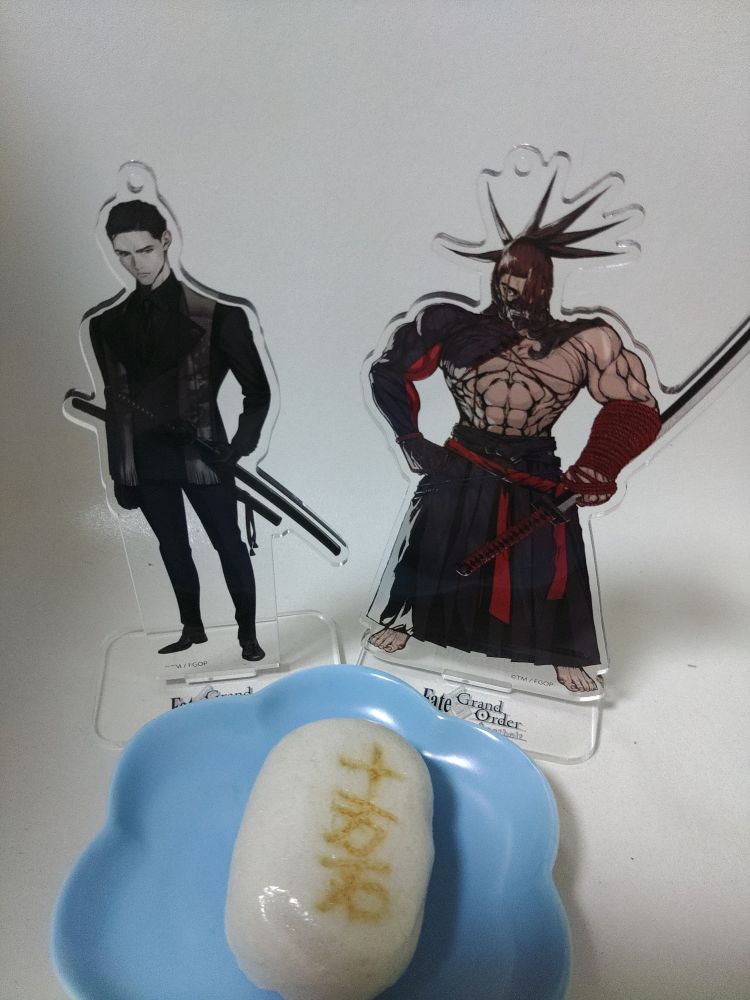 皿に乗った十万石饅頭とその奥に武市と田中のアクスタが並べられている