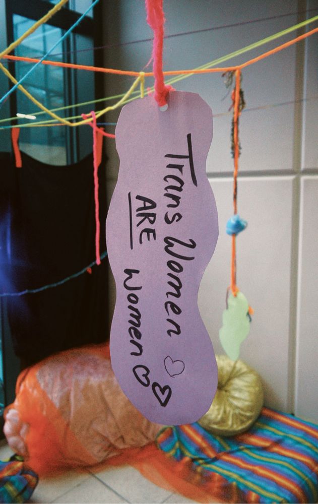 A paper sign hanging from the ceiling saying “Transwomen are women”. 