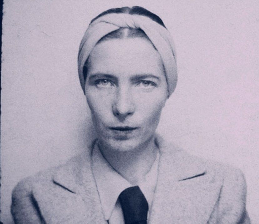 A black and white photo of young Beauvoir looking impossibly cool in a man's coat and a tie