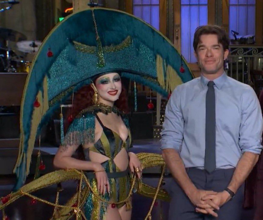 Chappell Roan in a really cool and colourful cunty harlequin type outfit next to John mulaney in a boring suit
