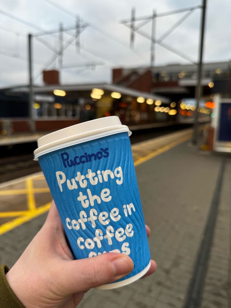 Bright blue textured coffee cup with Stevenage station in the backing. featuring text “Puccinos
Putting the coffee in coffee cups.”
