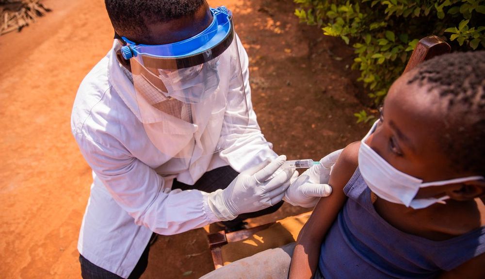 health worker in face shield and surgical mask gives a vaccine to a child
