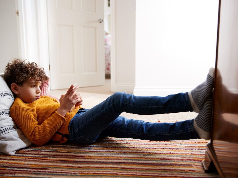 A kid using a phone while lying on his back