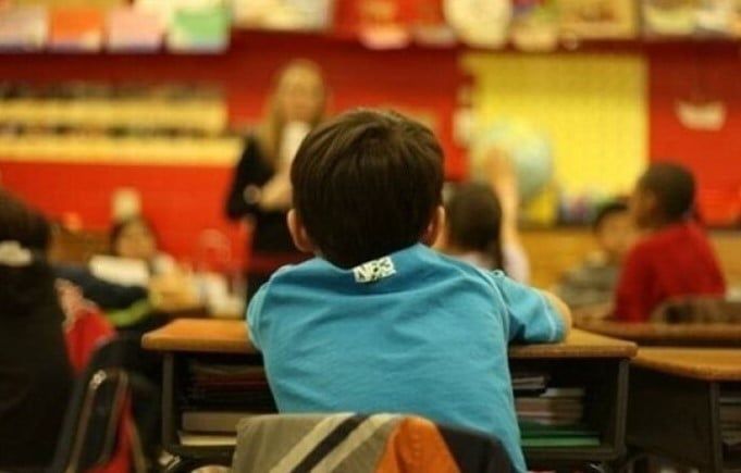 A child sits at a desk in a school classroom