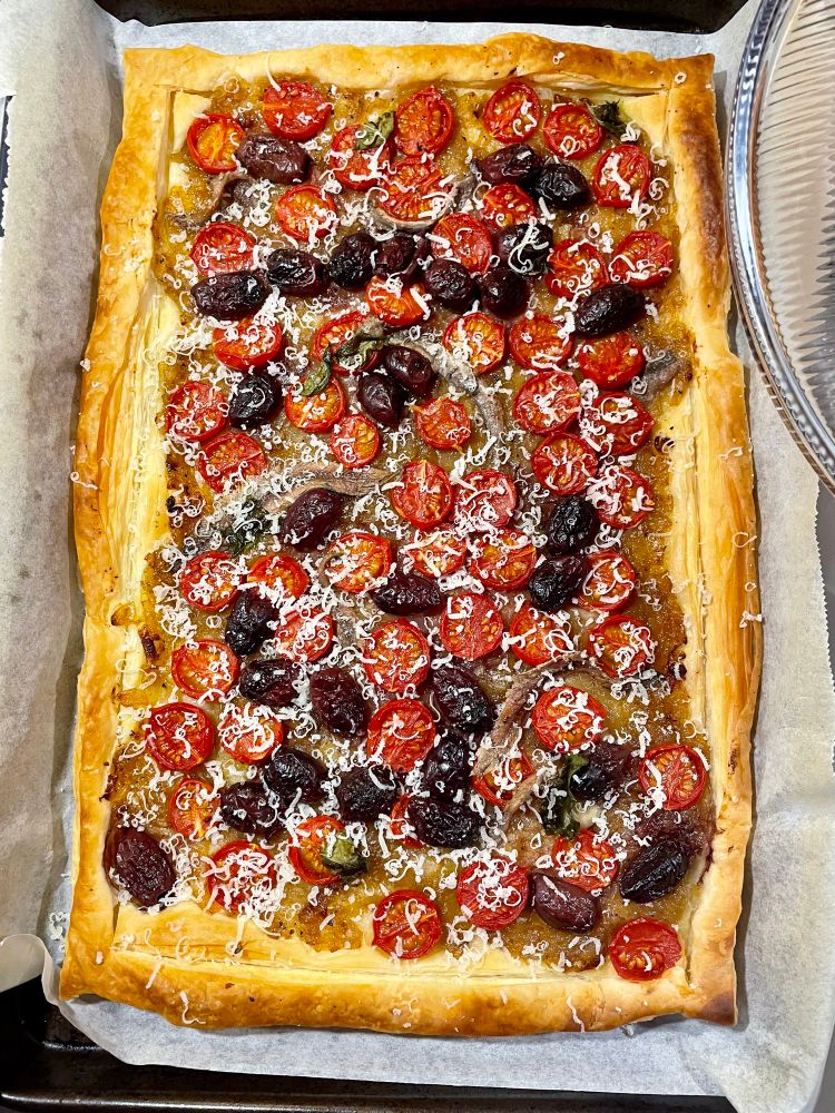 A baked pastry sheet topped with tomatoes, olives, anchovies and parmesan 