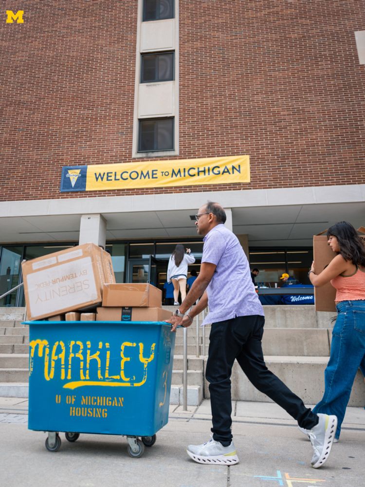 A family moving a blue bin into South Quad in front of a banner that reads "Welcome To Michigan."