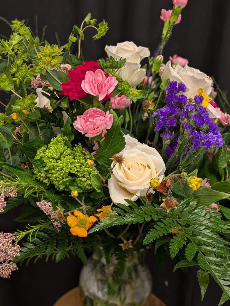 Bouquet of flowers and greens made with white roses, pink carnations, green hydrangea, and purple flowers. 