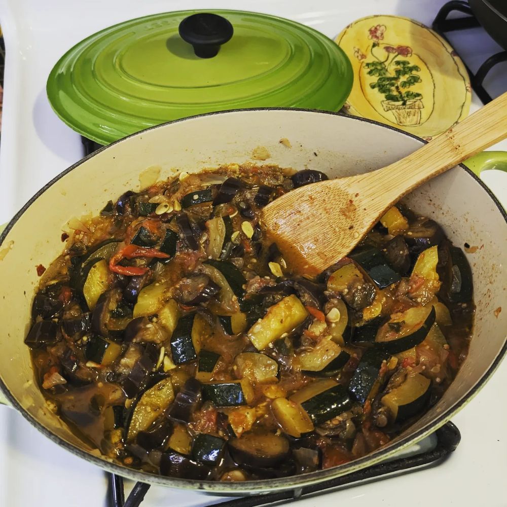 Cooked ratatouille in an oval dutch oven with a wooden spoon.