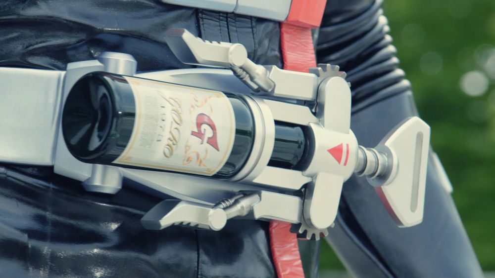 a zoomed-in picture of a belt on a black leather clad body (kamen rider g). the belt is a wine opener with a bottle in it with a large red "g" on it.