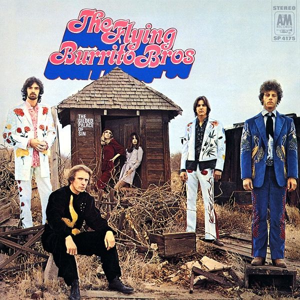 album cover for the flying burrito brothers' 1969 album "the gilded palace of sin"—the four members of the flying burrito brothers are standing (with one member sitting) in a brush and debris-filled desert with a small wooden shack in the background labeled "the gilded palace of sin*, with two women standing in it.