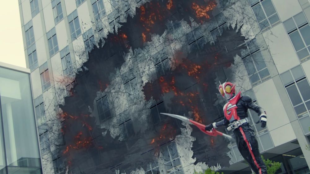 kamen rider g standing in front of a large building with the shape of his "g" logo blown out of it from an explosion. he is standing in the lower right corner holding his red and silver sword (it's shaped like an exacto blade).