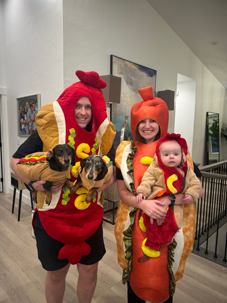 Two adults, a baby, and two dachshunds dressed up as hot dogs 🌭. 