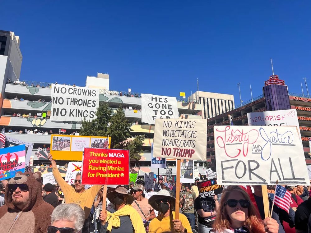 NO KINGS Protest in Reno, Nevada 10-18-25. They have banners which are 2.5 stories tall which they have draped from the top of a parking garage. One says " NO CROWNS, NO THRONES, NO KINGS". The other sign says, "HE'S GONE TO FAR".  
