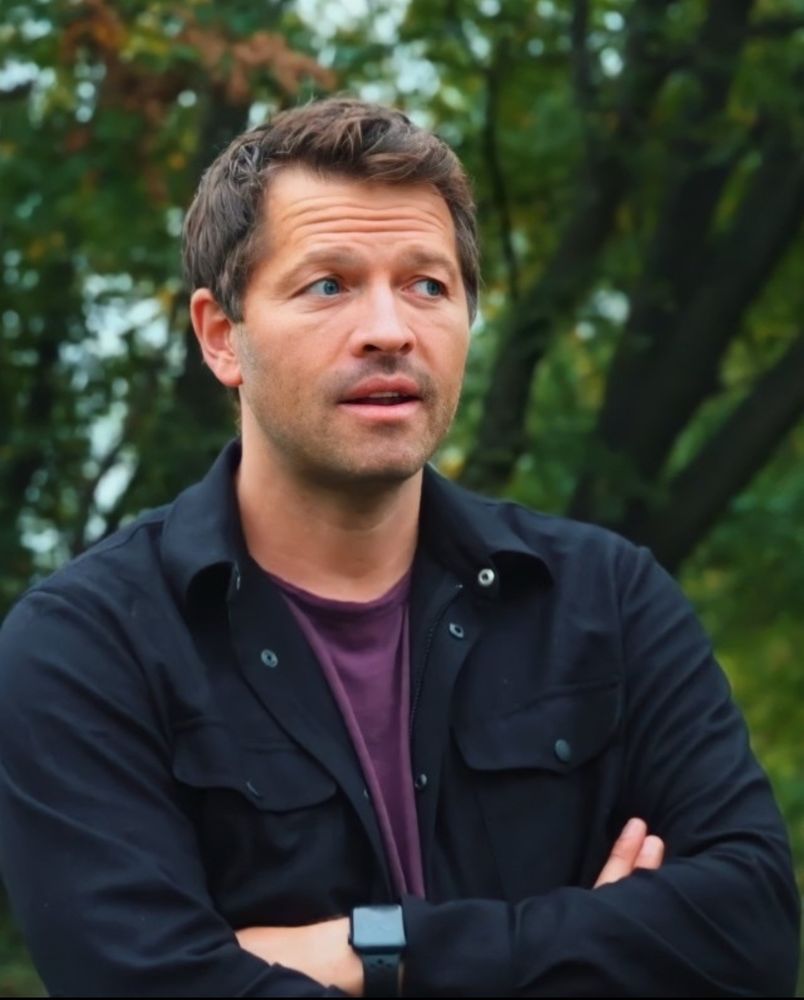 Misha Collins standing in front of trees 