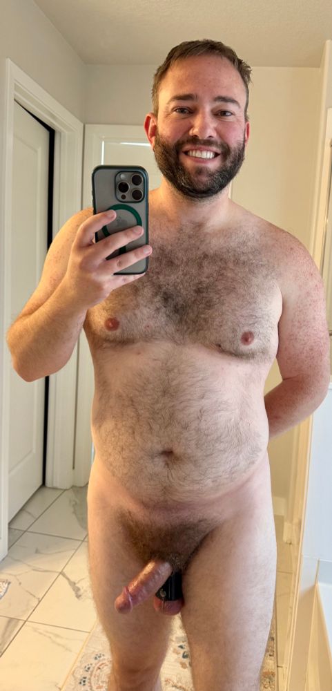 NSFW- full body view of naked hairy man. Dick is greasy and semi hard. Balls are in a ballstretcher