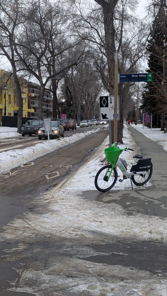 In a wintery scene, a Lime bike is parked near the 83rd Ave bike lane.