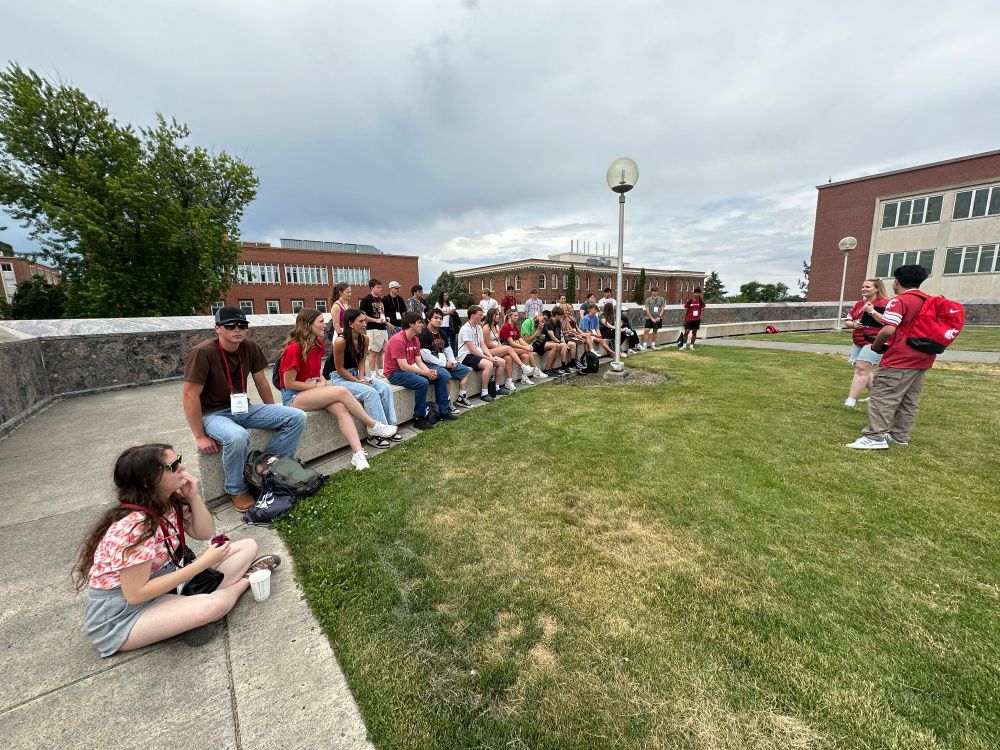 Color outdoor photo showing new students sitting and watching a presenter. 