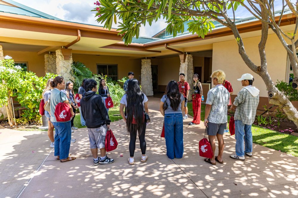 Color outdoor photo of a group of people standing in a circle outside a building 
