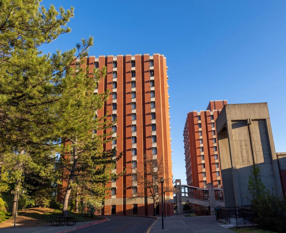 Color outdoor photo showing a red brick tower with green trees and blue sky above