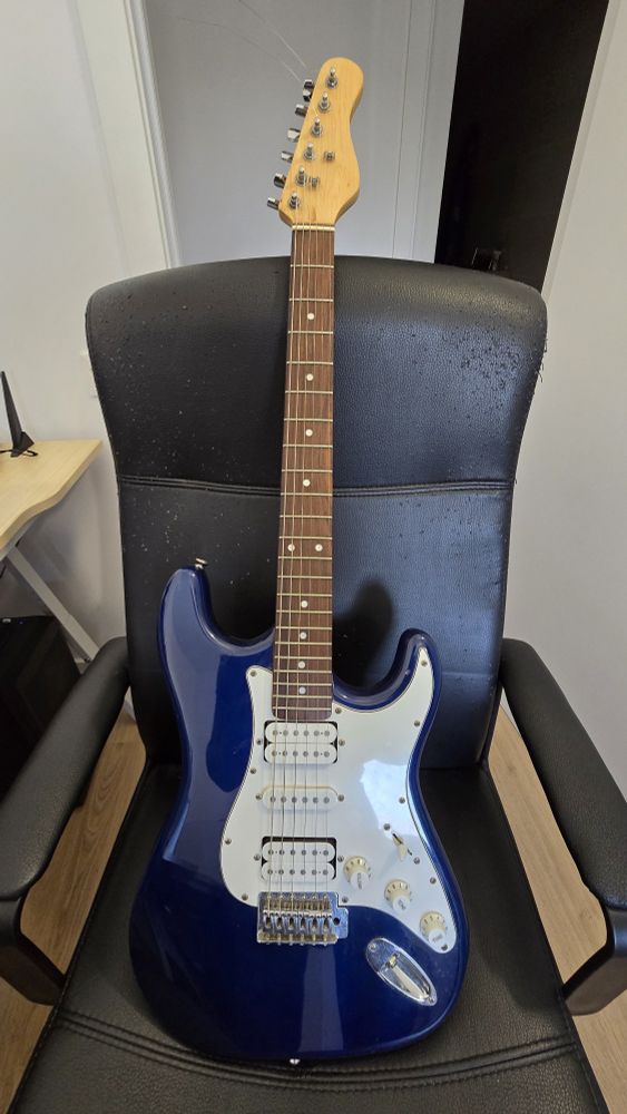 The whole guitar sitting on a chair. The top guitar tuner on the headstock is bent out of place.