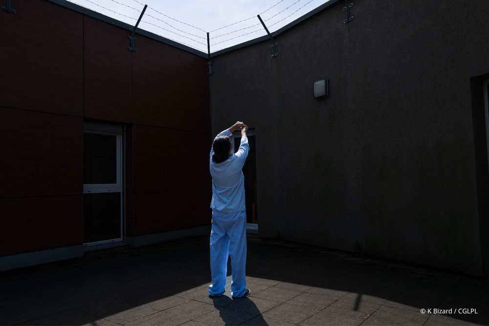 Patient en pyjama désignant les barbelés dans la cour d’un hôpital psychiatrique 