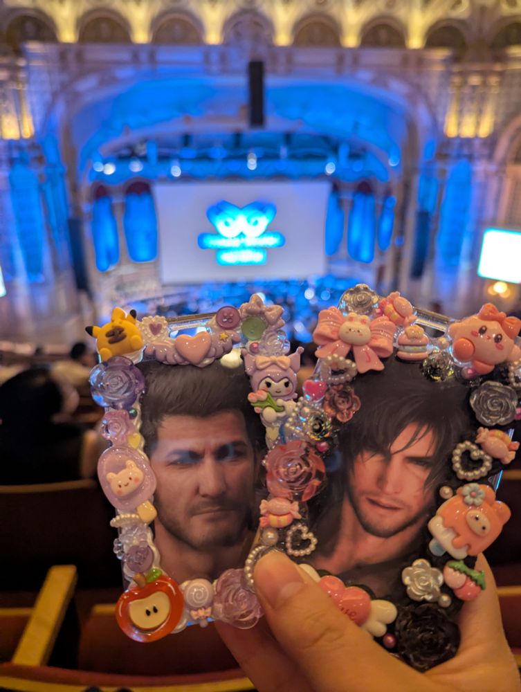 photo of two decoden photocard holders, one of cidolfus telamon and the other of clive rosfield, held up against an out of focus view of the distant worlds concert logo