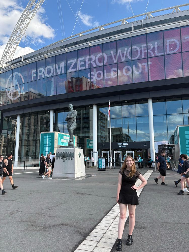 Tegan stood infront of Wembley stadium, the text reads ‘from zero world tour, sold out’ 